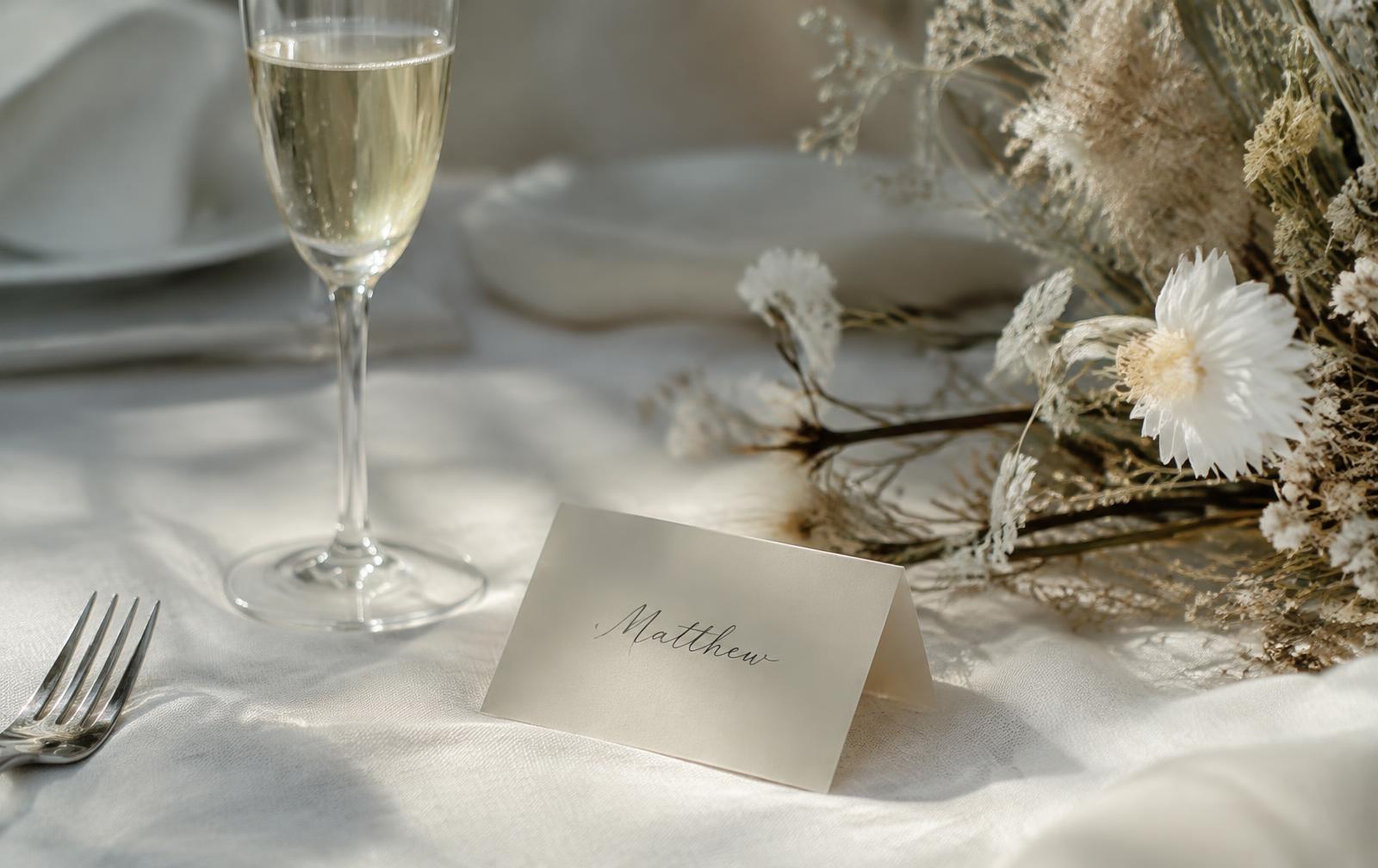 Hand-written place card beside champagne and dried flowers